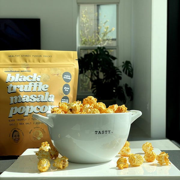 White bowl of black truffle masala popcorn with popcorn bag behind it