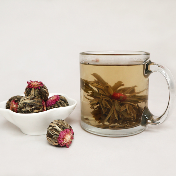 Small dish of jasmine tea balls beside glass with blooming jasmine tea ball in water